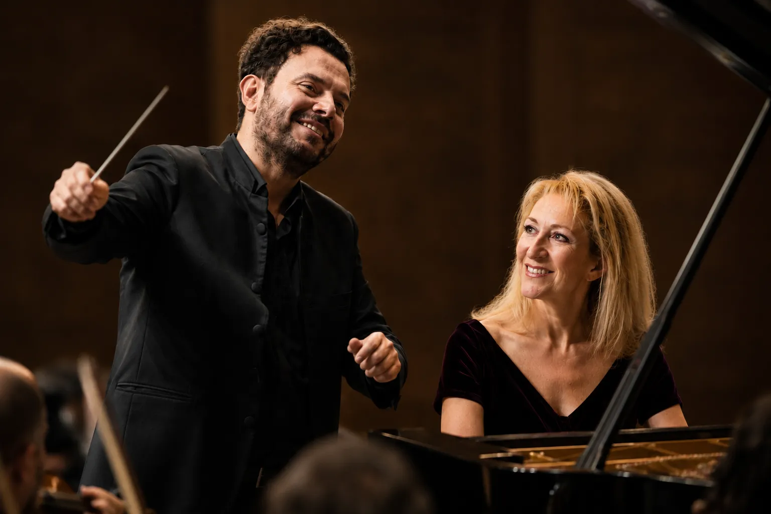 Conductor Michalis Oikonomou leads the orchestra while pianist Natalia Michaïlidou performs at the piano in a warm concert hall setting, promoting the Athens State Orchestra's performance of Shostakovich's Symphony No. 10.