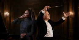 Conductor Yoav Talmi and pianist Isata Kanneh-Mason in a premium editorial portrait for the Athens State Orchestra's 7th concert of the 2026–2027 artistic season, presented as a seamless photographic composite inside an elegant European concert hall with warm cinematic lighting inspired by Beethoven's