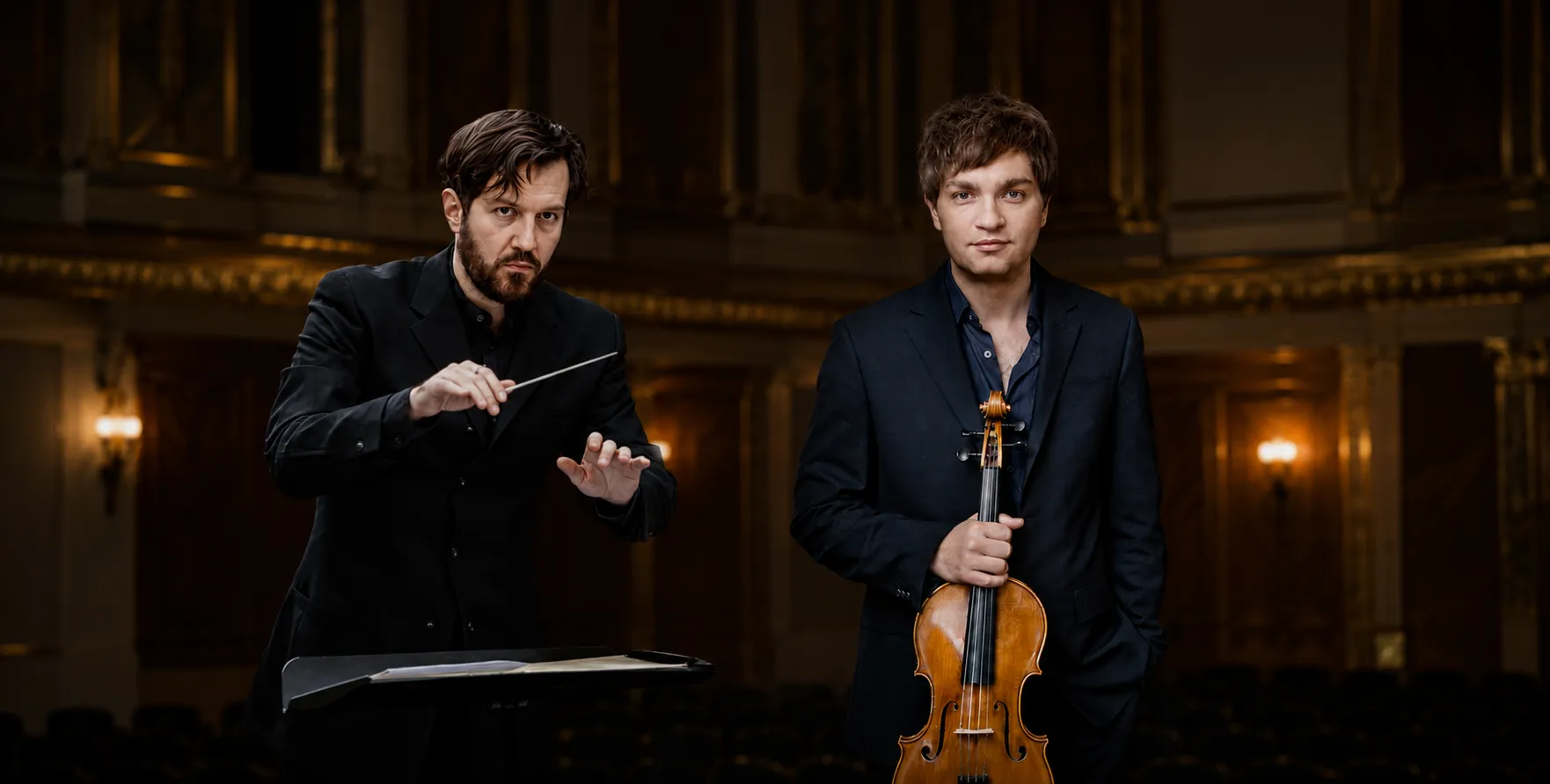 Conductor Giorgos Ziabras and violist Nils Menkemayer in a cinematic concert hall portrait, standing side by side against a warm, elegant orchestral backdrop.
